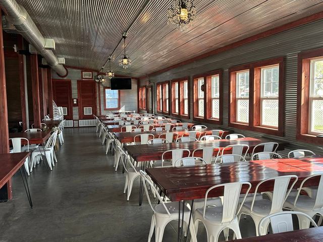 Bright barn hall with long tables, white chairs and a row of windows along the wall