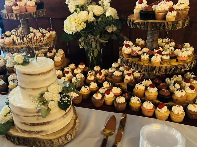 Tiered white wedding cake decorated with fresh flowers next to cupcakes on display stands