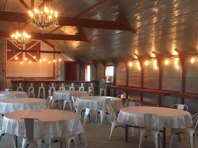 Round tables with white cloths and white chairs under chandeliers and warm string lights
