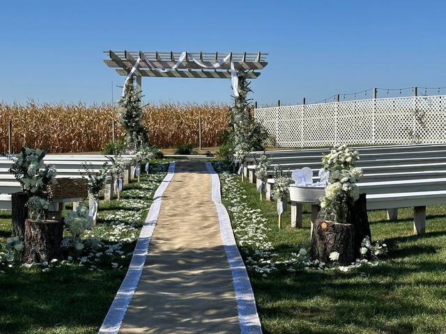 Outdoor wedding aisle under a white arbor decorated with florals, with a green cornfield behind