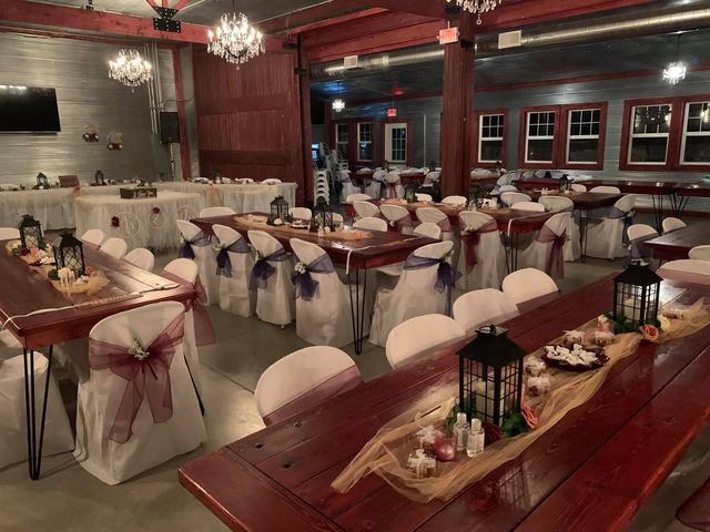 Wooden farm table with draped chair covers, lanterns and rustic food boards in a red barn