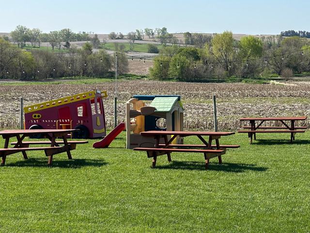 Outdoor play area with a red slide and wooden picnic tables on a green lawn