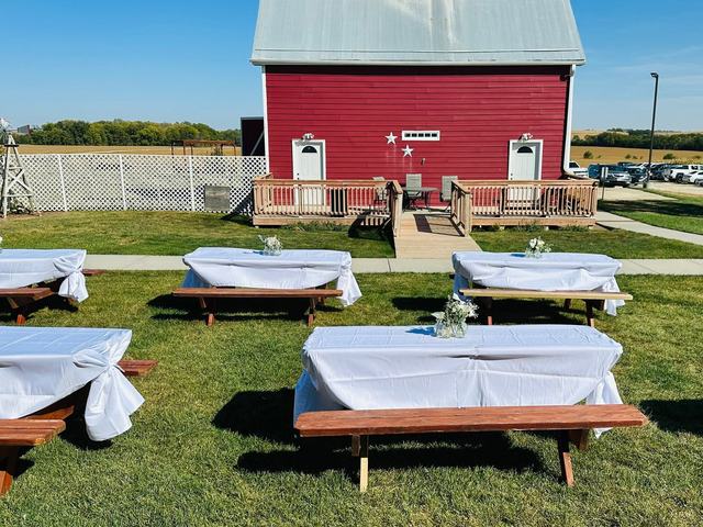 Red barn with long tables covered in white linens set out on a green lawn