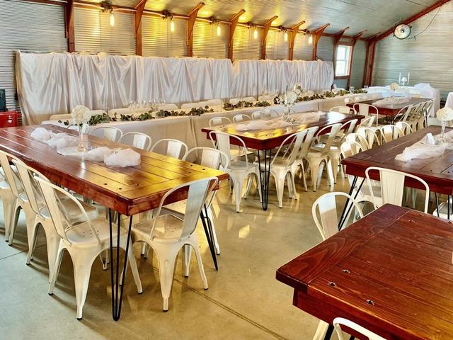 Warmly lit hall with long wooden tables, cream metal chairs, and a white-draped head table
