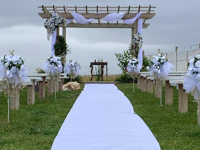 Garden-style wedding arch decorated with white flowers and a long white aisle runner on green grass