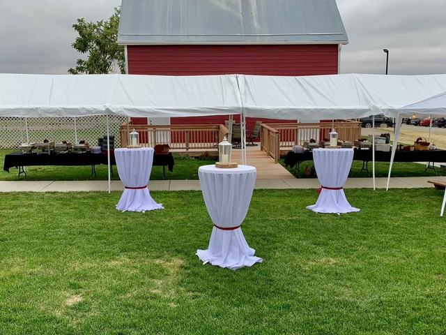 White event tent over lawn with draped cocktail tables and a red barn behind
